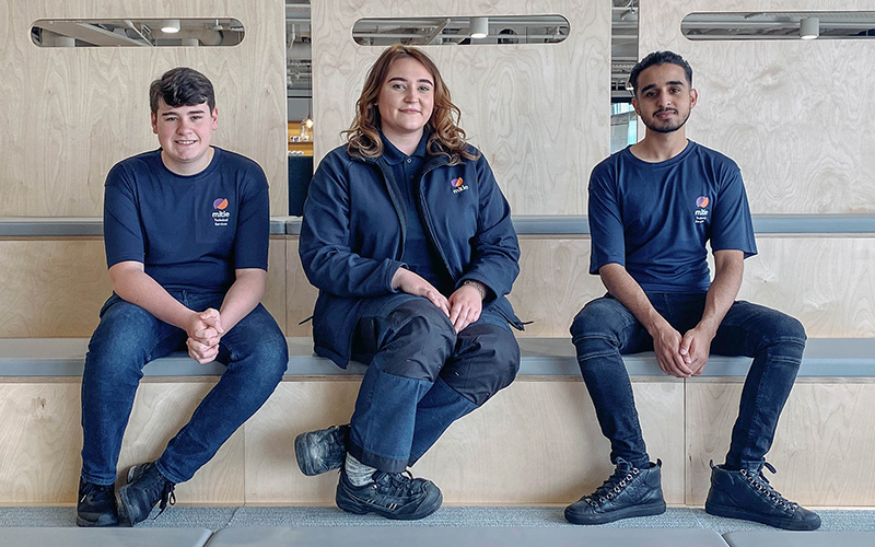 Three apprentices sitting on a bench in Mitie uniform