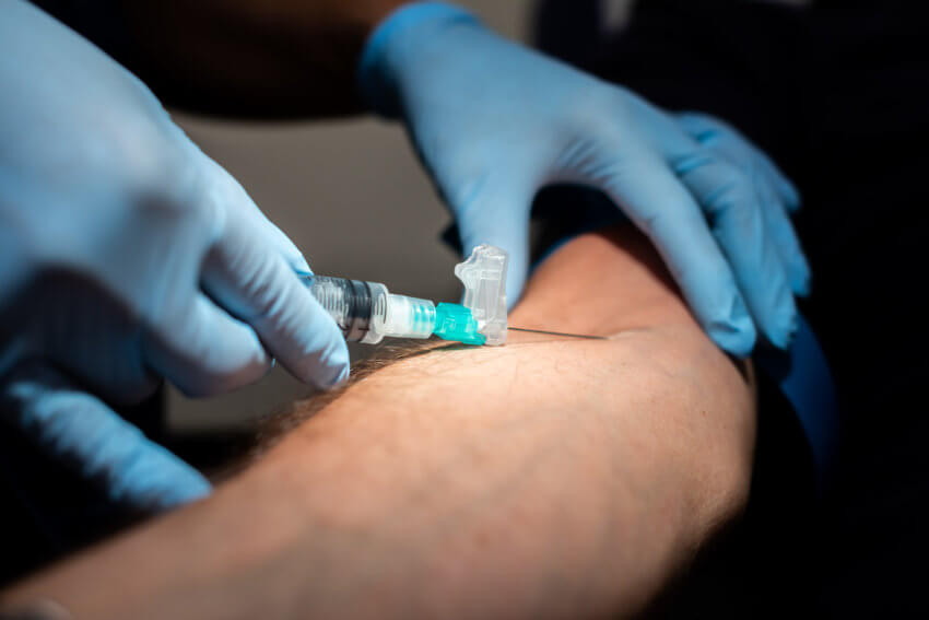 A close-up of a syringe being inserted into a male white patient's arm