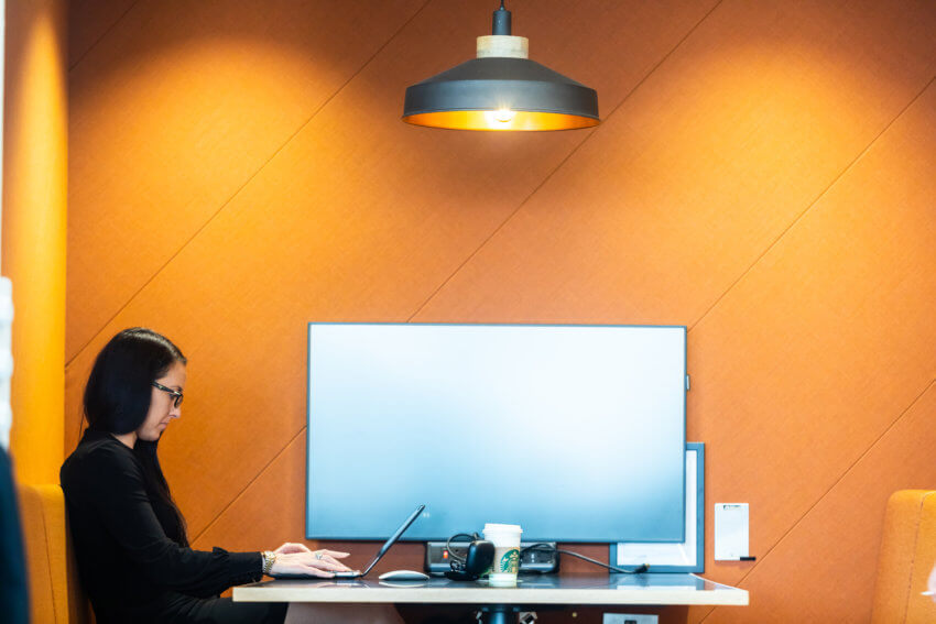 Mitie employee working on a laptop in an orange-coloured booth, with a screen on the wall