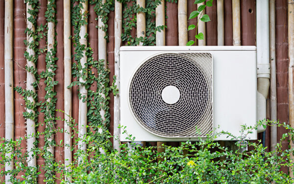 A white air conditioning unit mounted on a wall with greenery surrounding it