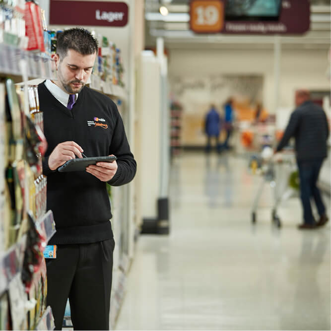 A Mitie security guard in a Sainsbury's store using a mobile reporting device