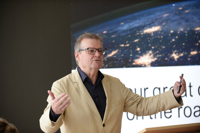 Antony Slumbers, in a tan suit and dark shirt, gesturing in front of a presention slide at a Mitie Estate Optimisation event