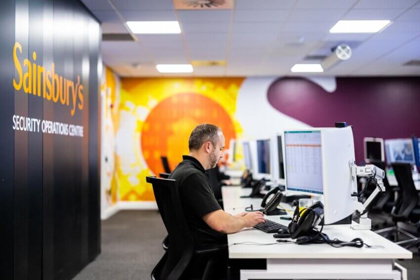 Mitie employee at a computer in the Security Operations Centre, with Sainsbury's branding on the walls