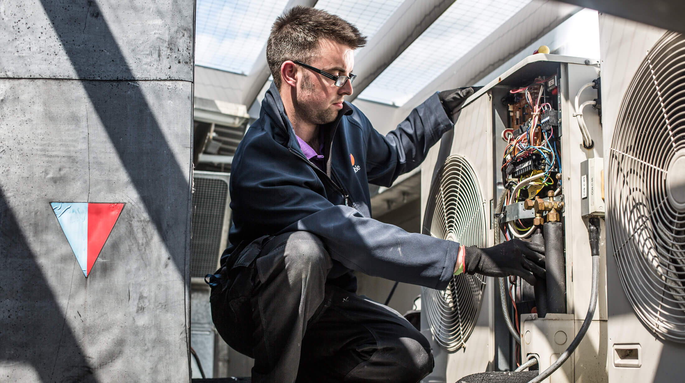 Mitie engineer kneeling on the floor while working on an air con unit