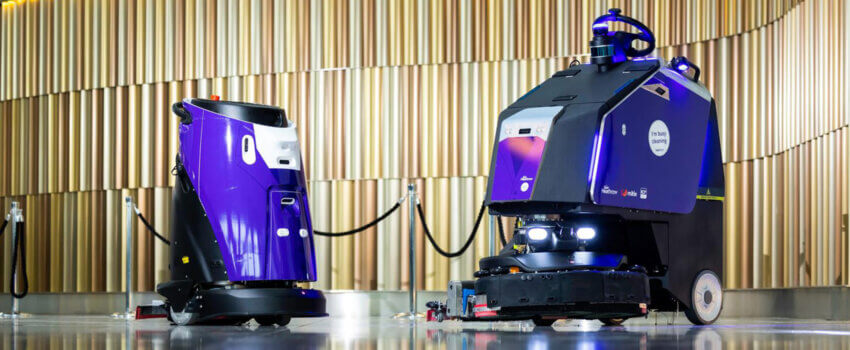 Two cleaning robots, painted purple, in a terminal at Heathrow Airport