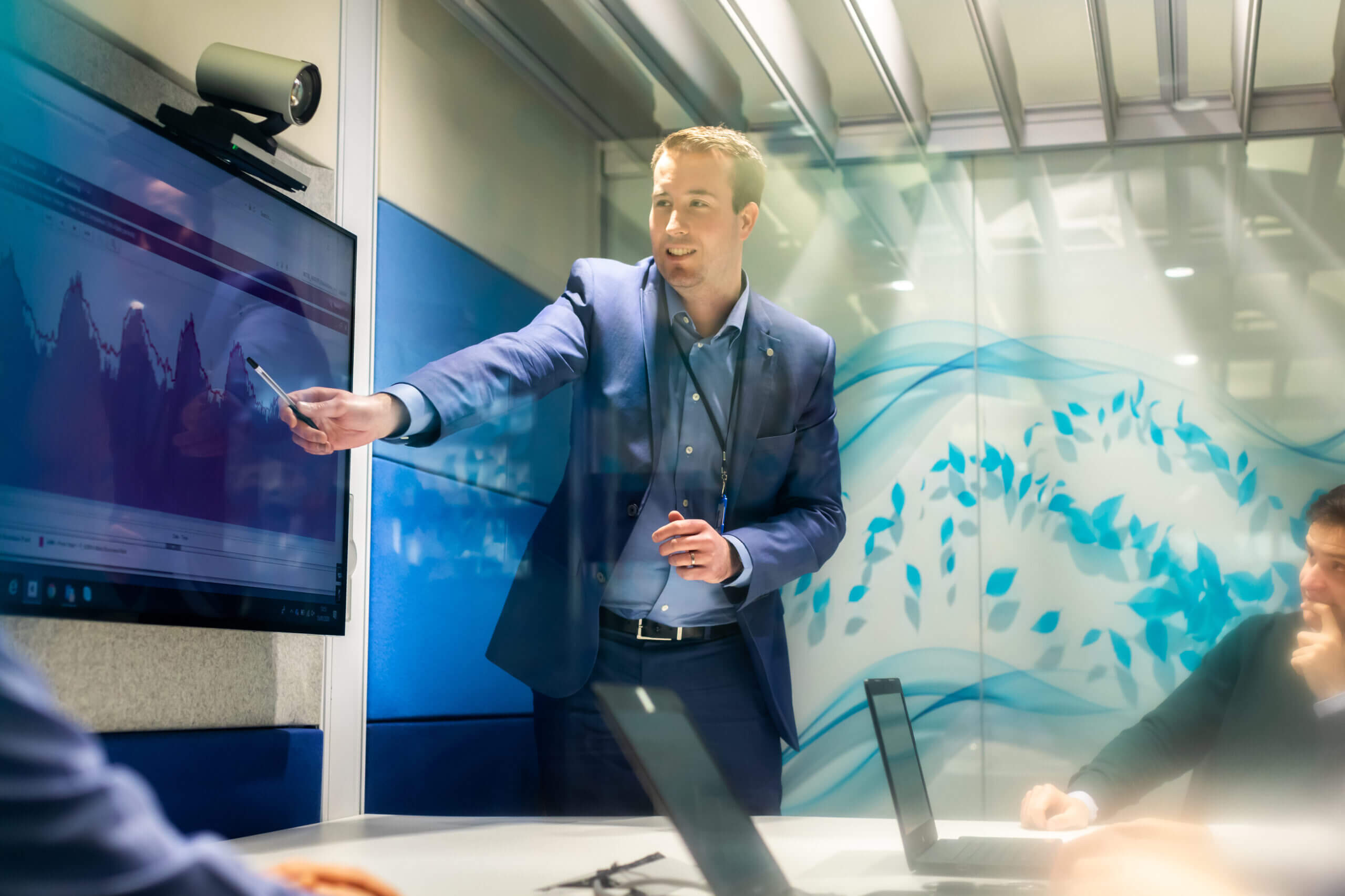 Man wearing a blue suit giving a presentation, pointing at some interesting data on the screen behind him